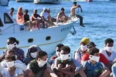 TOPSHOT - Migrants rescued by Italys' Guardia Costiera ( Coast Guard ) sits as a boat with tourists enter...